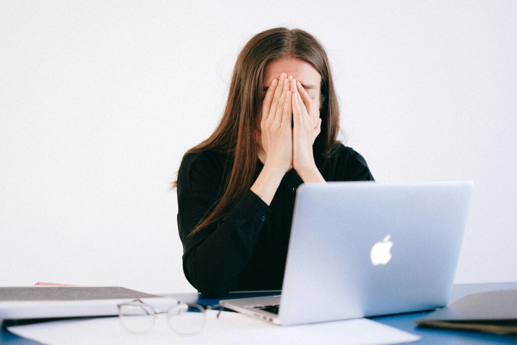 stressis inimene hoidmas käsi näo ees ja sülearvuti lauataga